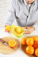 Young man using citrus-fruit squeezer, preparing orange juice