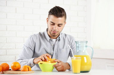 Young man using citrus-fruit squeezer, preparing orange juice