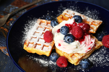 Sweet homemade waffles with forest berries and cream on plate, on dark wooden background