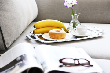 Light breakfast and magazines on sofa in living room, close up
