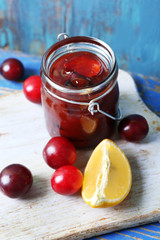 Tasty homemade plum jam in glass jar on wooden background