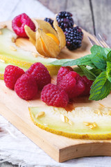 Berries, mint and melon on wooden cutting board