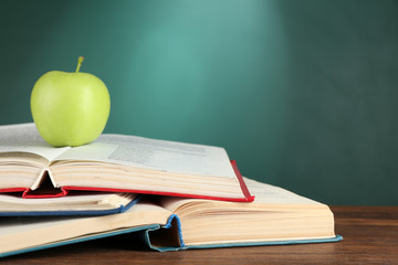Open books and green apple on desk on green chalkboard background