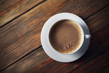 Cup of coffee with foam on wooden table, top view