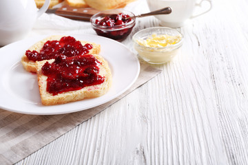 Bread with butter and homemade jam in plate on wooden background