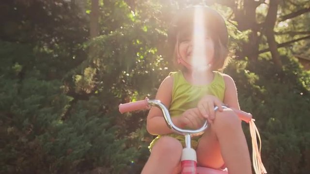 An adorable little girl sitting on her tricycle and smiling
