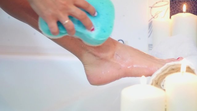 sexy woman washing legs in bath with blue sponge on burning