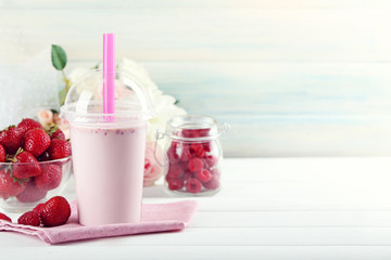 Plastic cup of milkshake on light wooden background