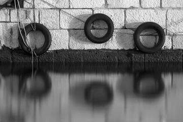 Crédence de cuisine en verre imprimé Noir et blanc Vieux pneus automobiles utilisés comme pare-chocs sur le quai de la mer. Photo longue exposition en noir et blanc.