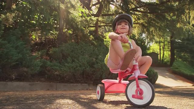 An adorable little girl sitting on her tricycle and fixing her shoe
