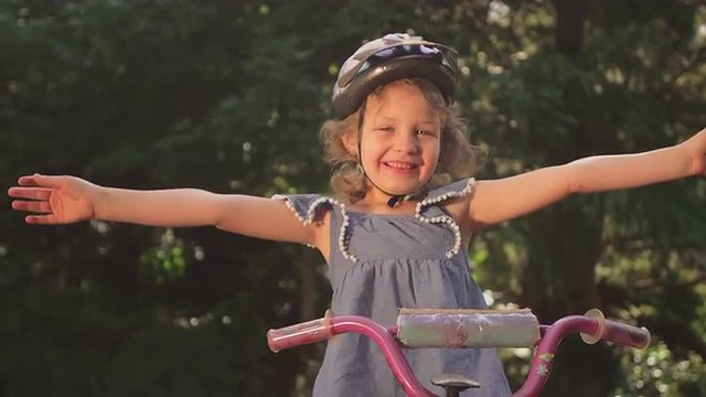 A little girl on a bike stretches her arms out and smiles