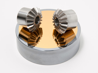 Bevel gear-wheels on a golden mirror isolated against a white background