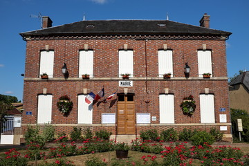 façade de mairie en brique rouge avec ciel bleu et drapeaux français.