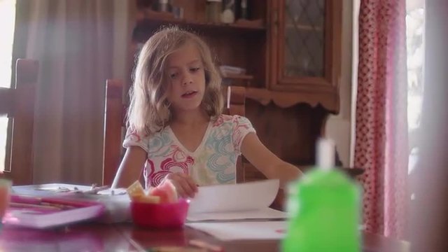 A little girl sitting at a table and coloring with crayons

