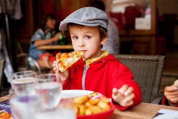 Sweet adorable child, boy, eating pizza at a restaurant