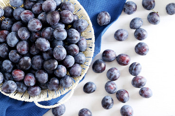 Fresh plums in basket on white wooden background