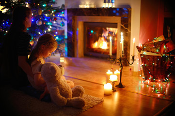 Young mother and daughter sitting by a fireplace on Christmas