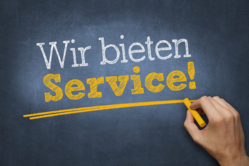 Hand schreibt mit Kreide Text "Wir bieten Service!" auf Tafel
