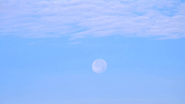 Moon moves across blue sky with beautiful cirrus clouds