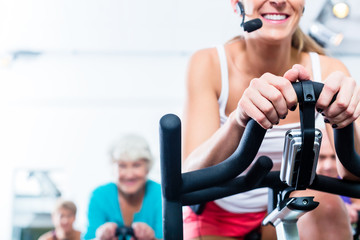 Fototapeta na wymiar Senioren beim Spinning auf Fitness bike mit Trainer