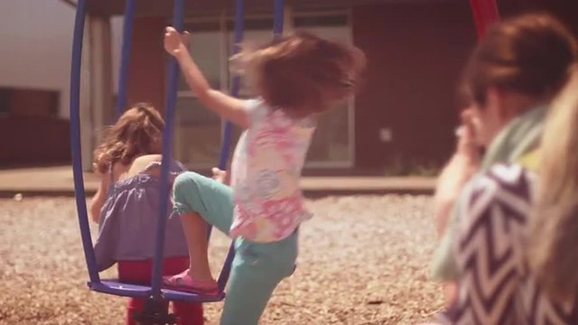 A mother takes pictures of her daughters spinning on a play structure
