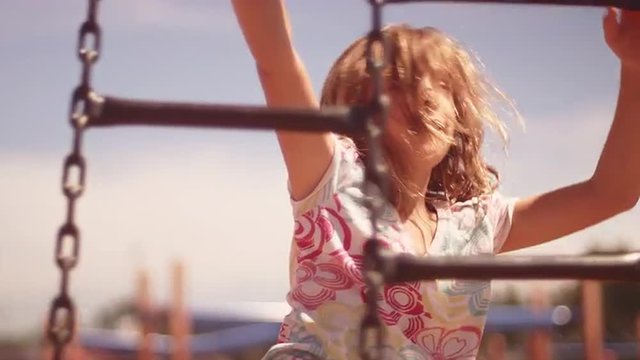 A young girl climbs across some hanging ladders at a playground