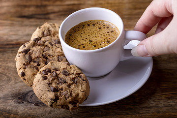 cup of coffee with chocolate cookies and female hand on wood
