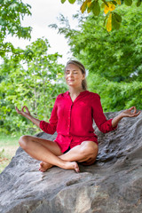 Naklejka na ściany i meble outdoors meditation - smiling young yoga woman escaping in closing eyes,relaxing in sitting in lotus pose on a big stone, summer daylight