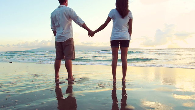 Attractive Young Brunette couple holding each other. romantic in love kissing at beach sunset. Newlywed happy young couple enjoying ocean sunset during travel holidays vacation getaway. 