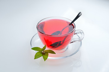 Hibiscus tea glass cup on a saucer with mint leaves and spoon