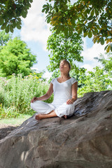 outdoors zen exercise - focused young yoga woman escaping in closing eyes,relaxing bare feet on a big stone, summer daylight