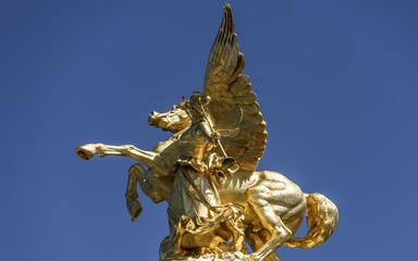 Bronze statue of Pegasus and angel, against pure blue sky, Pont Alexandre III and the dome of Les Invalides (Paris, France).