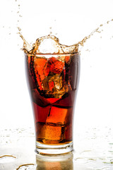 Ice cube droped in cola glass and cola splashing