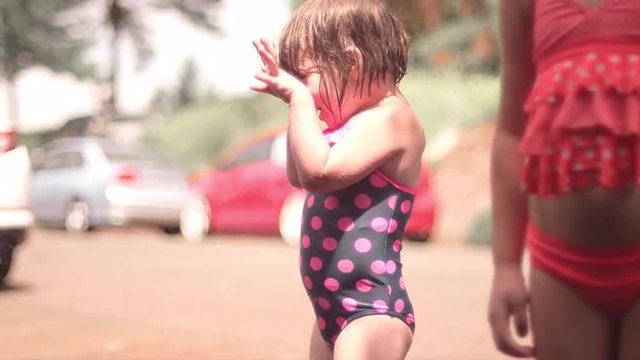 A cute little girl being sprayed with a hose and running away

