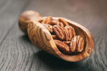 pecan nuts in olive wood scoop on oak table