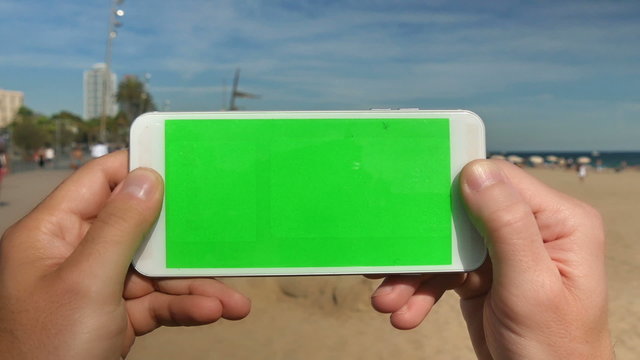 5186 Holding a green screen smartphone at the beach.	