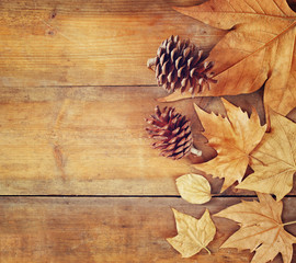 top view image of autumn leaves and pine cones over wooden textured background