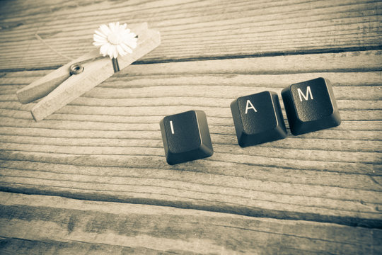 "I am" wrote with keyboard keys on wooden background, sepia effe