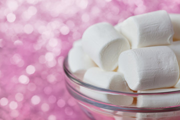 White soft marshmallows in glass bowl with pink bokeh background, selective focus