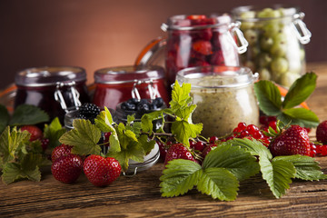 Jams in glass jars with wood and fresh berries 