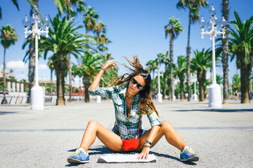 Beautiful young cheerful girl is sitting down around the palm trees looking at the touristic map guide in a sunny day in Barcelona - 90826146