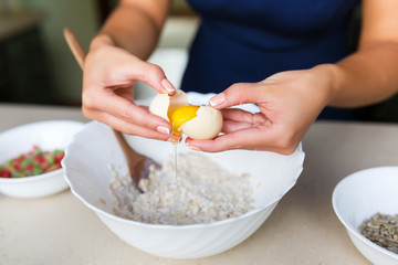 Young woman breaks the egg in the dough