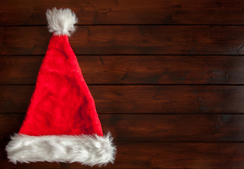 Obraz na płótnie Canvas Red Santa Hat with white fur trim on dark brown wooden floorboards. Copy space for Christmas greeting.