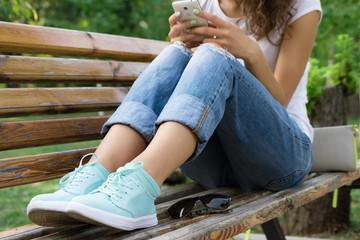 Girl in jeans sits on a park bench and using a mobile phone