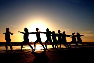 Fototapeta na wymiar yoga group by the sea as silhouette at sunset