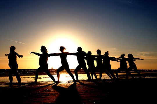 yoga group by the sea as silhouette at sunset