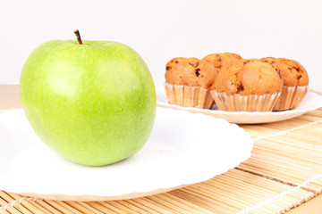 Apple and cakes in white plates on wooden mat