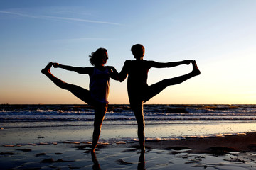 Fototapeta premium yoga at the beach by the sea with two woman as a silhouette
