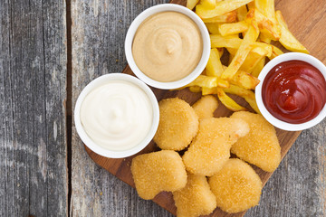 chicken nuggets with french fries and different sauces on board