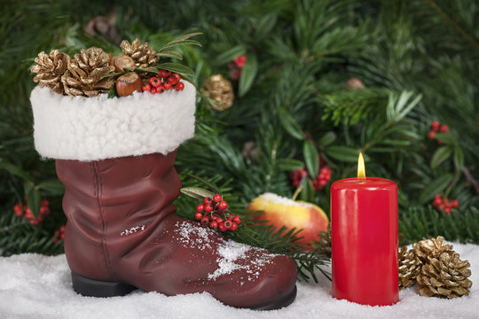Prall gefüllter Stiefel vom Weihnachtsmann auf Schnee im Hintergrund Tannenzweige